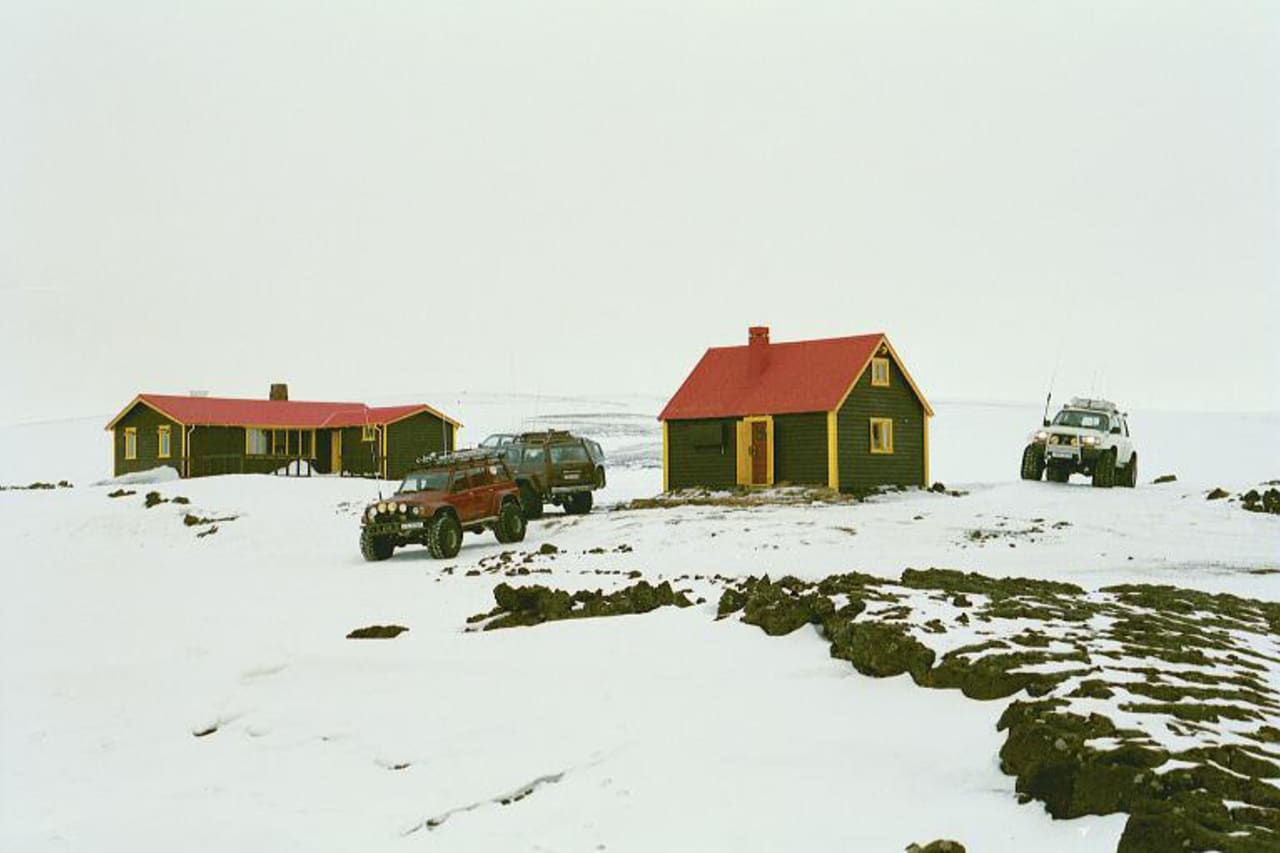 Jökulheimar huts with red roofs, snow-covered ground, and modified vehicles in the Highlands.
