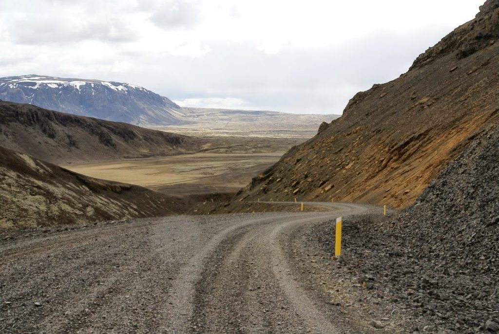 A narrow gravel section of the Kaldidalur road descending between dark volcanic slopes.