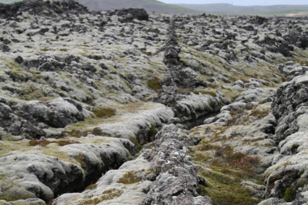 Close view of rough Kapelluhraun lava cracks and moss near the chapel-ruin area.