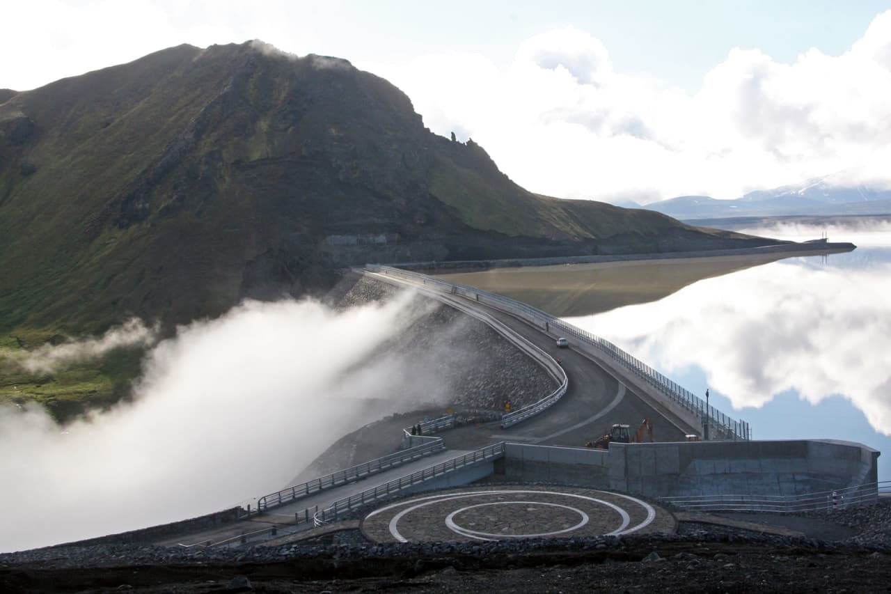 Kárahnjúkavirkjun dam spillway releasing water beside Hálslón reservoir and East Iceland highland mountains.