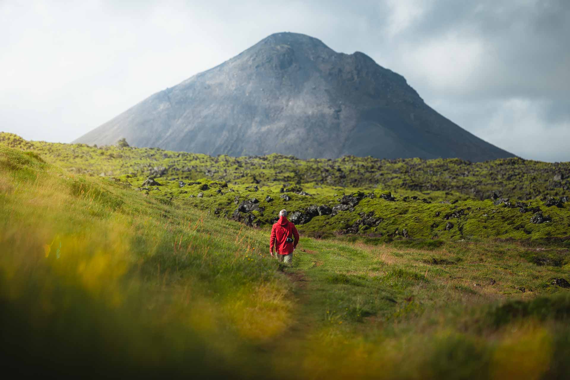 Hiker on the Keilir trail with the mountain rising ahead over green lava fields.