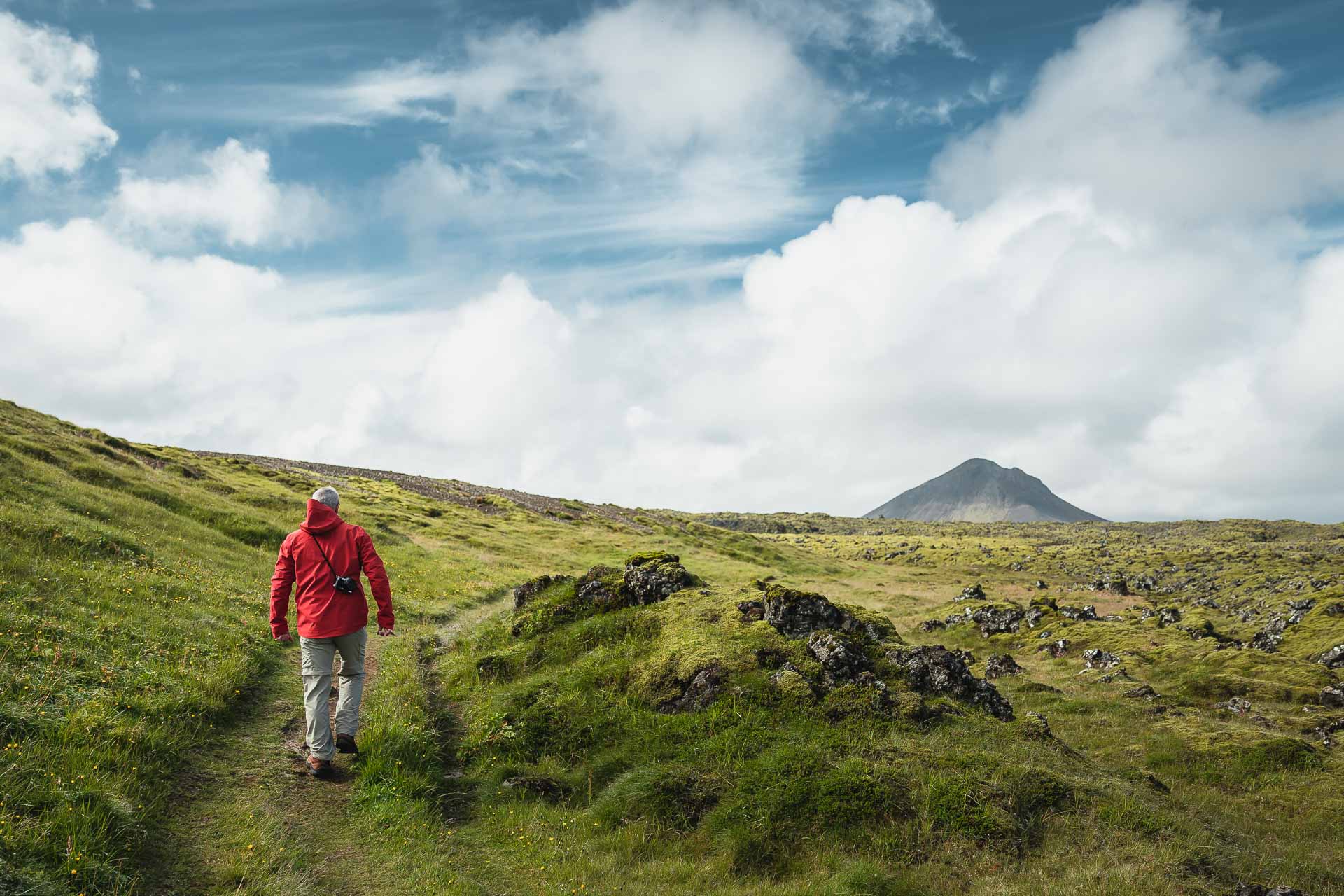 Hiker walking through mossy Reykjanes lava fields toward the cone of Keilir mountain.