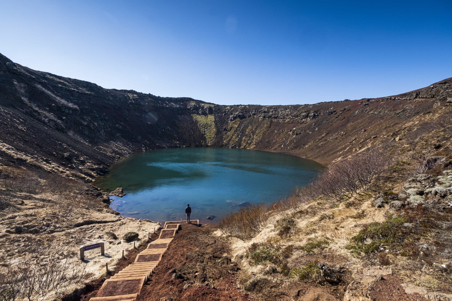 The lake-level stairs and blue-green water inside Kerið Crater, surrounded by red volcanic slopes.