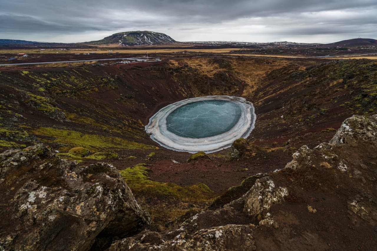 Kerið Crater in winter with snow on the volcanic slopes and the crater lake partly frozen.