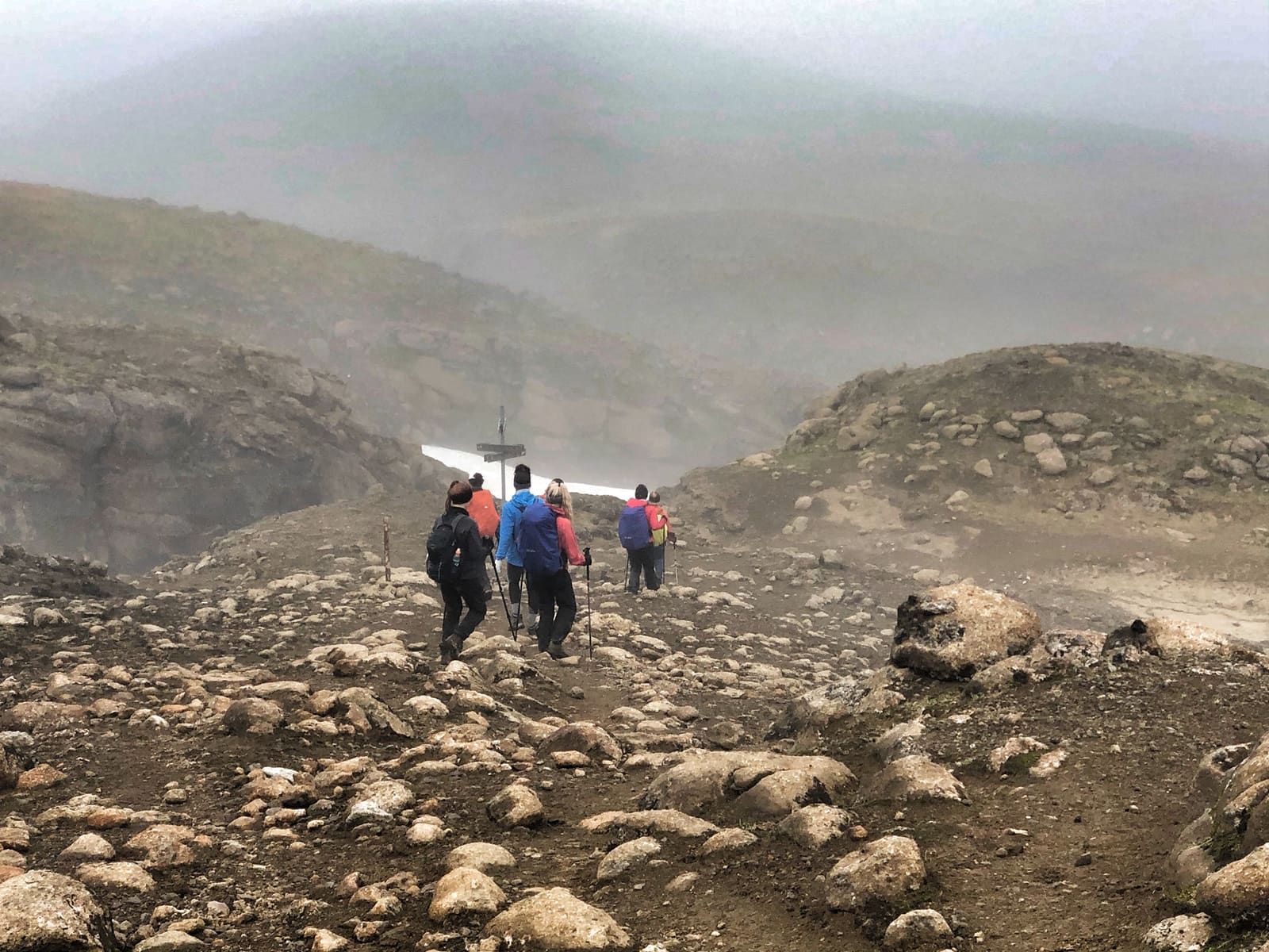 Hikers walking through Kerlingarfjöll on a marked highland path with snow-streaked mountains behind them.