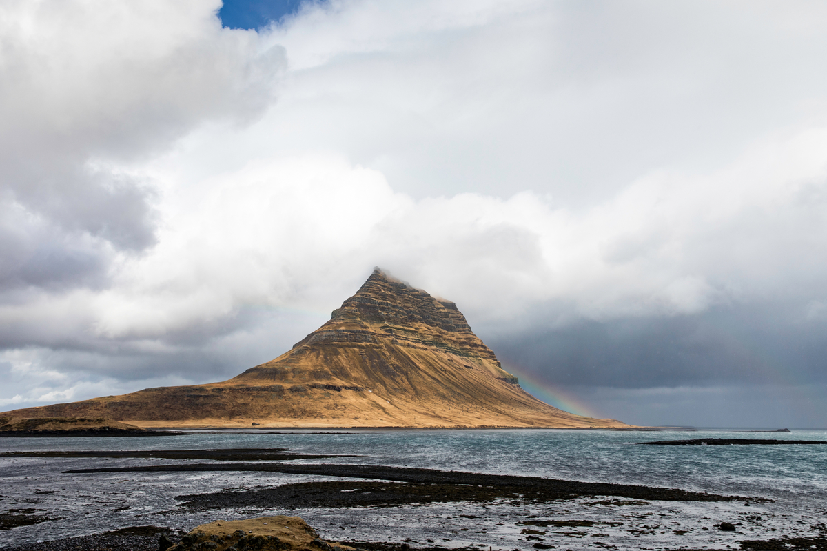 Kirkjufell mountain across the water with low cloud and a faint rainbow.
