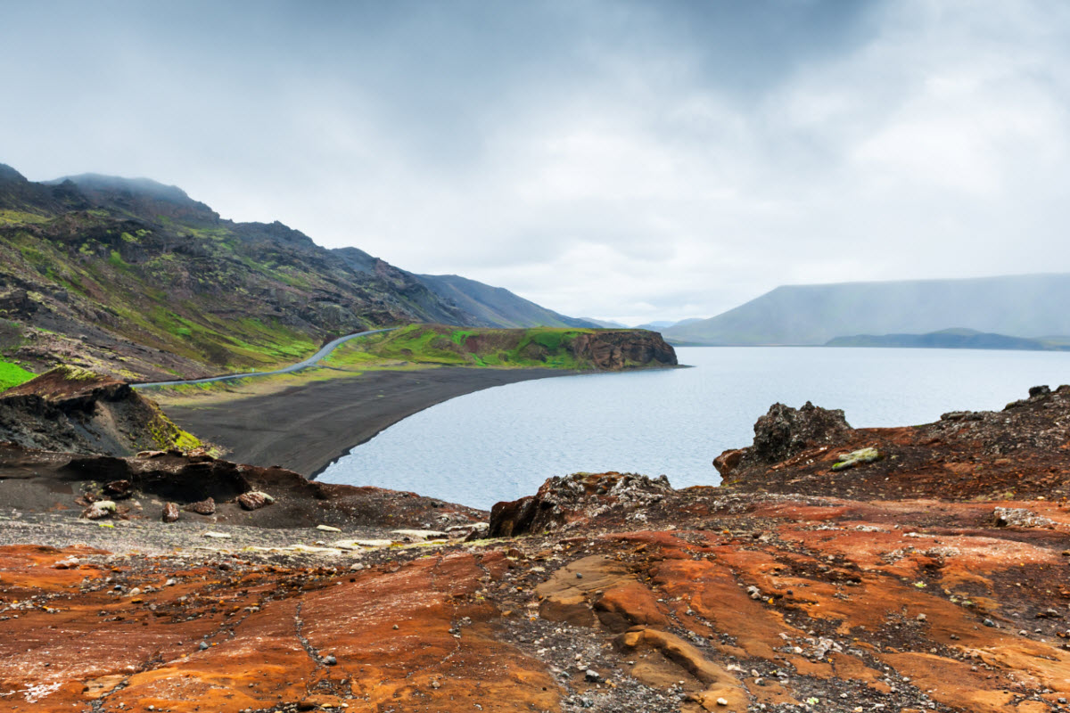 Red volcanic rocks, black shoreline, and pale lake water at Kleifarvatn on the Reykjanes Peninsula.