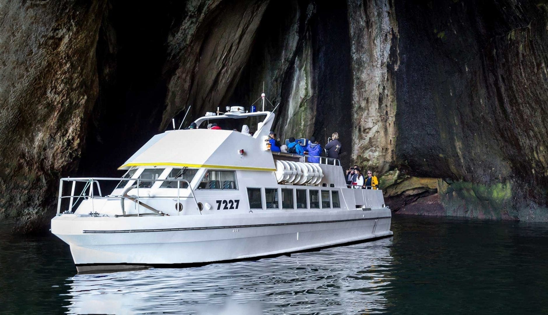 Sightseeing boat floating inside the dark Klettshellir sea cave below high rock walls.