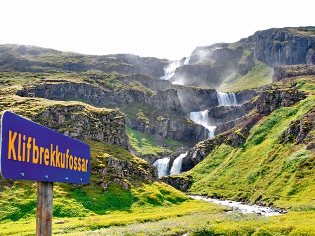 Blue Klifbrekkufossar roadside sign beside the tiered waterfall in Mjóifjörður.