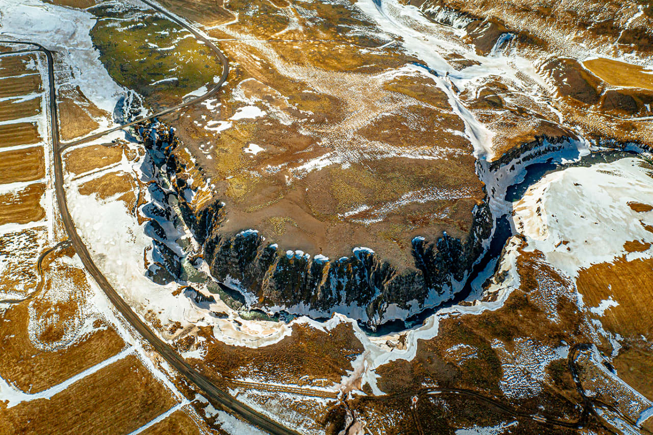 Aerial view of Kolugljúfur canyon cutting through snowy farmland beside Road 715.