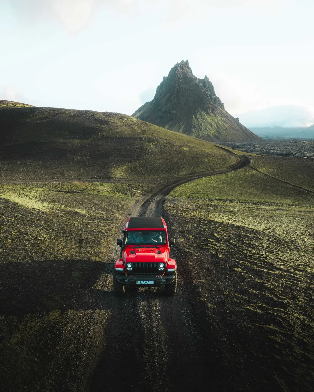 A red high-clearance vehicle on the rough track below the jagged Krakatindur mountain in the southern Highlands.
