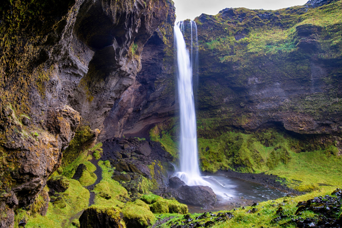 Kvernufoss falling into a green and dark rock canyon near Skogar.