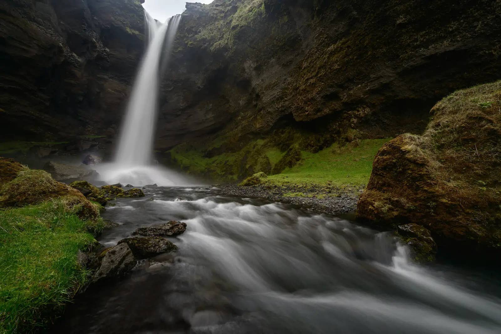 Kvernufoss dropping into a dark canyon stream below mossy rock walls.