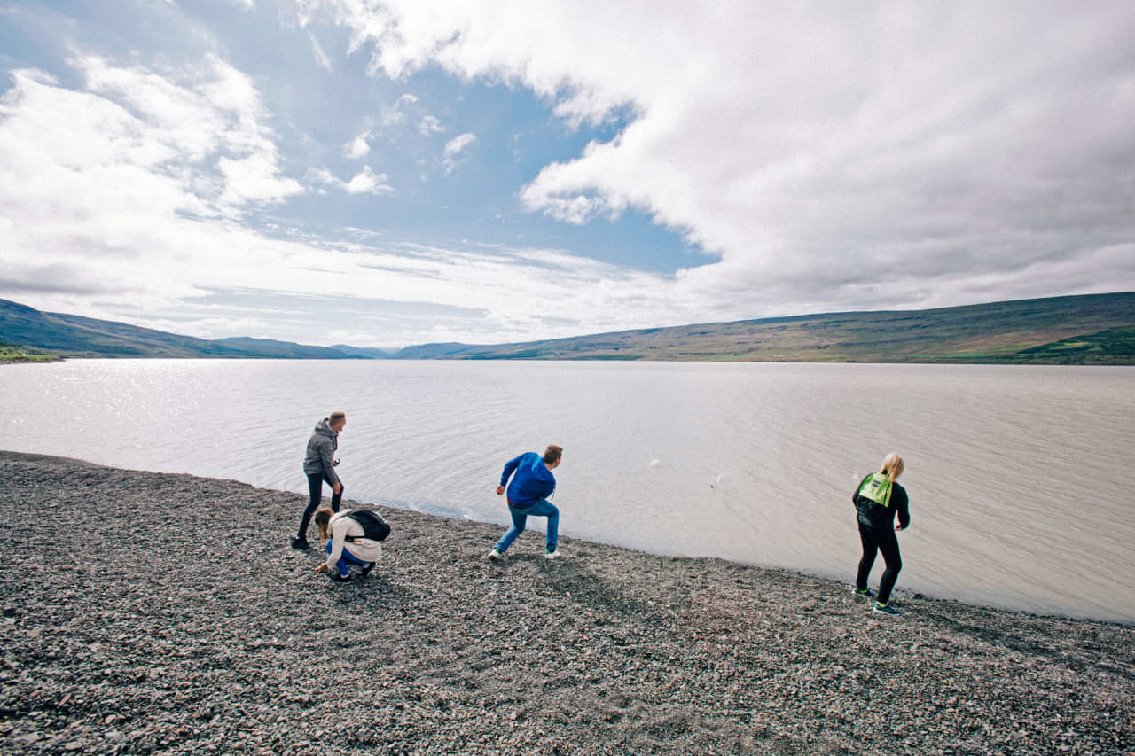 Travelers standing on the pebbled edge of Lake Lagarfljót under a cloudy East Iceland sky.