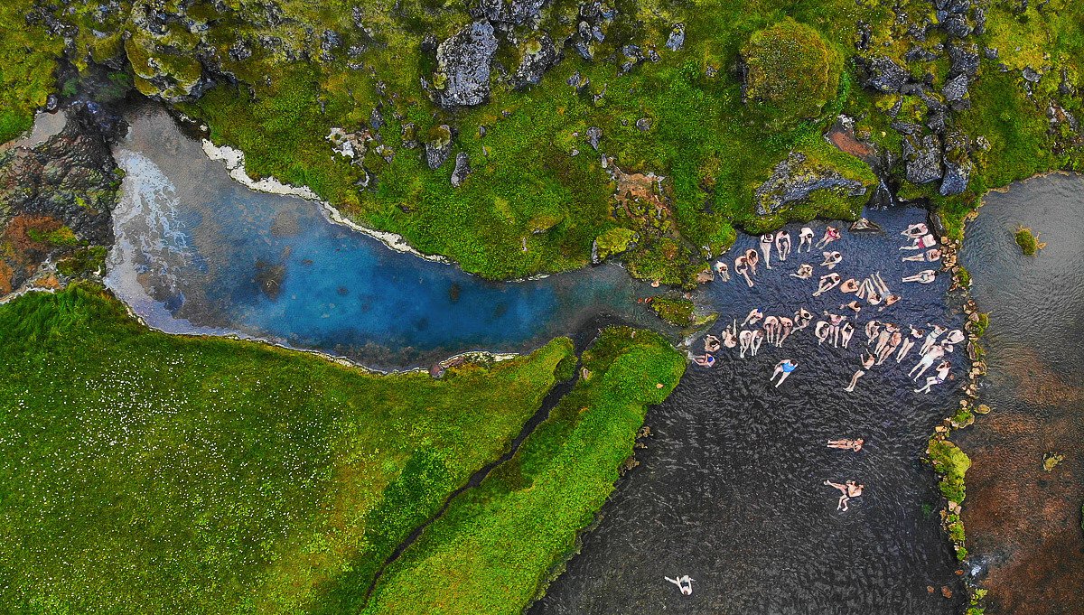 Aerial view of the Landmannalaugar bathing brook with people soaking beside green moss and dark water.