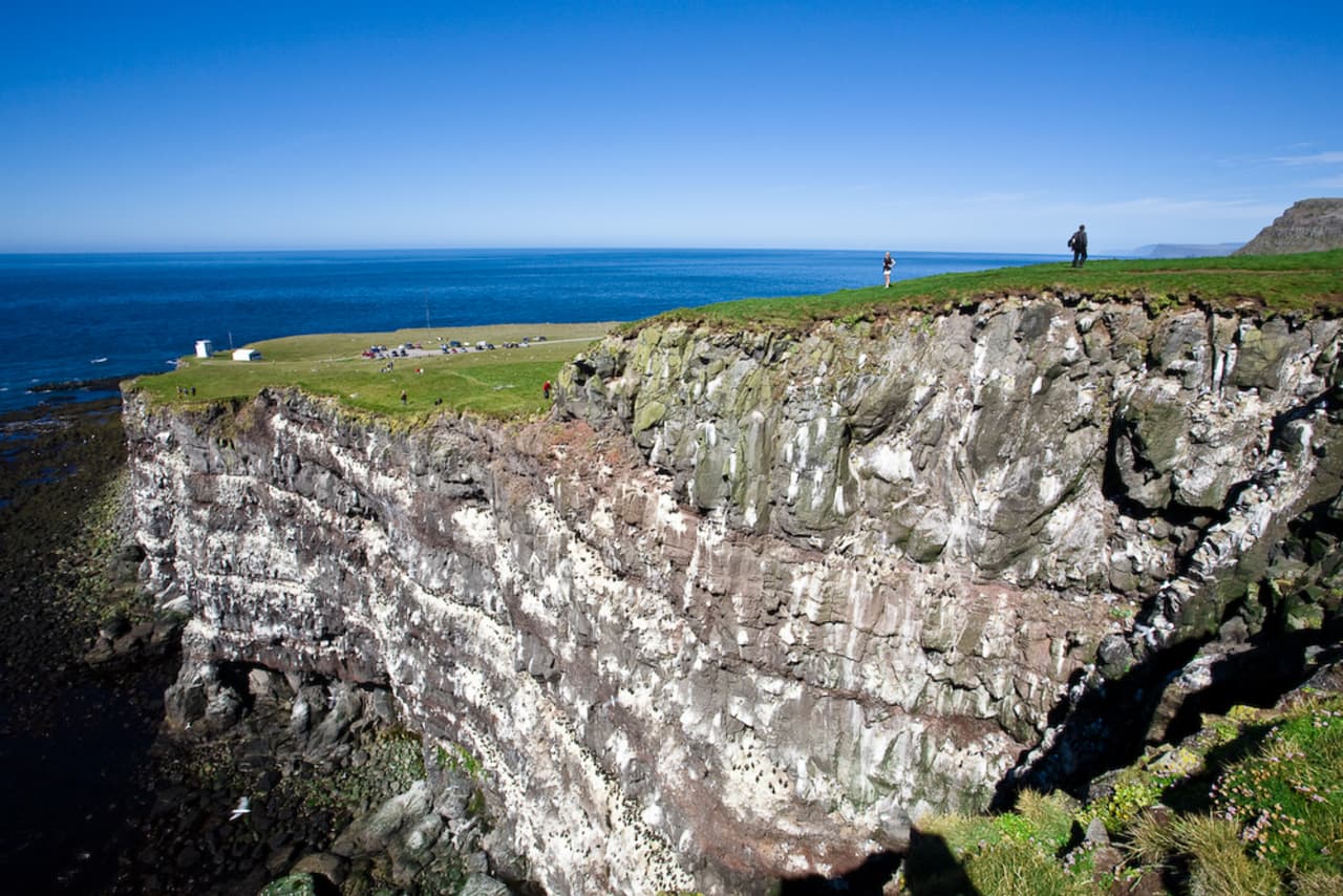 Látrabjarg cliff tops above the sea with Bjargtangar lighthouse visible in the distance.