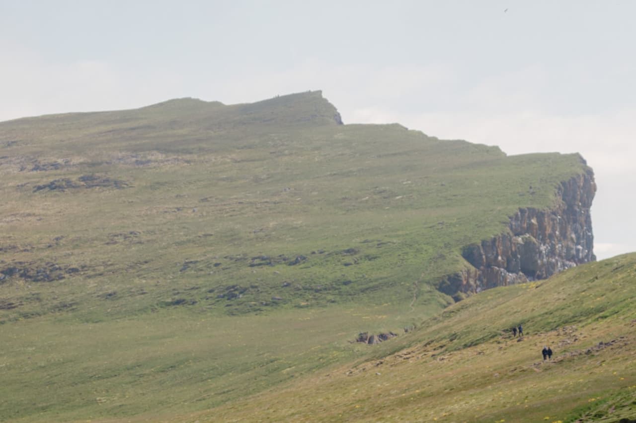 Hikers walking across grassy slopes toward the long cliff line at Látrabjarg.
