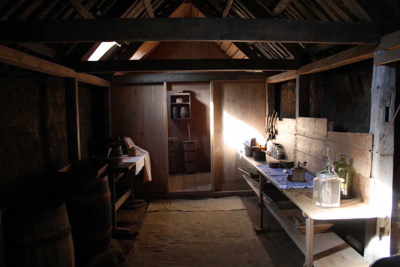 Wooden interior room at Laufás with turf walls, beams, shelves, and household objects.