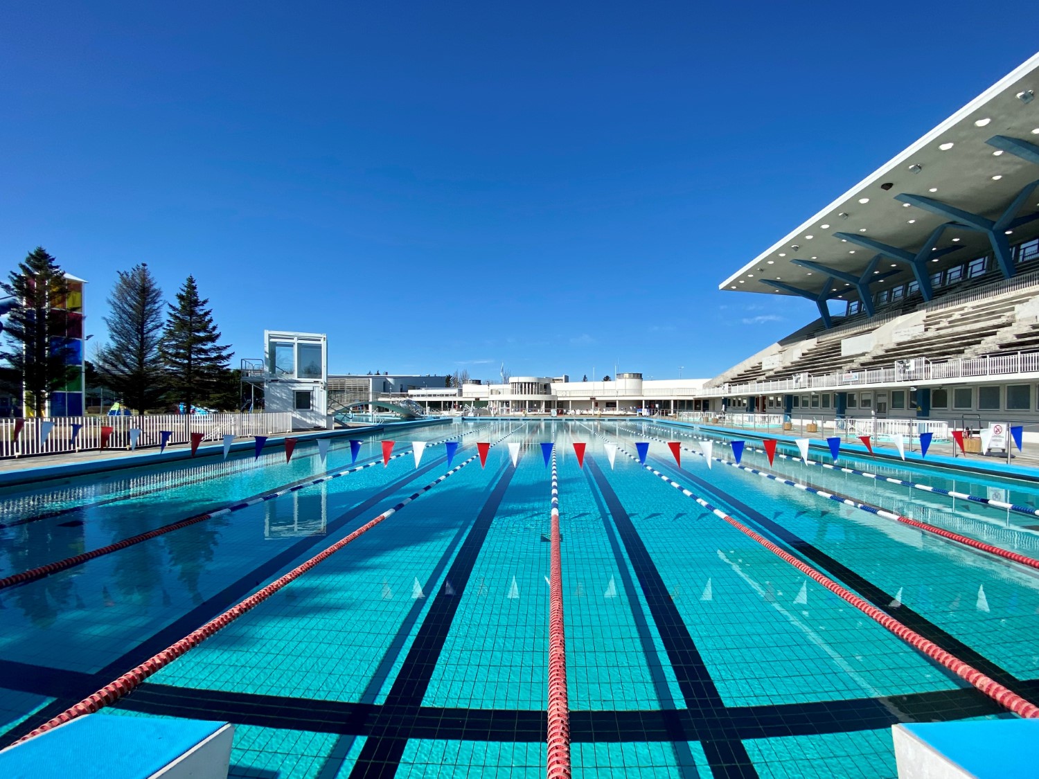 Outdoor lap pool at Laugardalslaug with the grandstand, slide tower, and main pool complex under a clear Reykjavík sky.