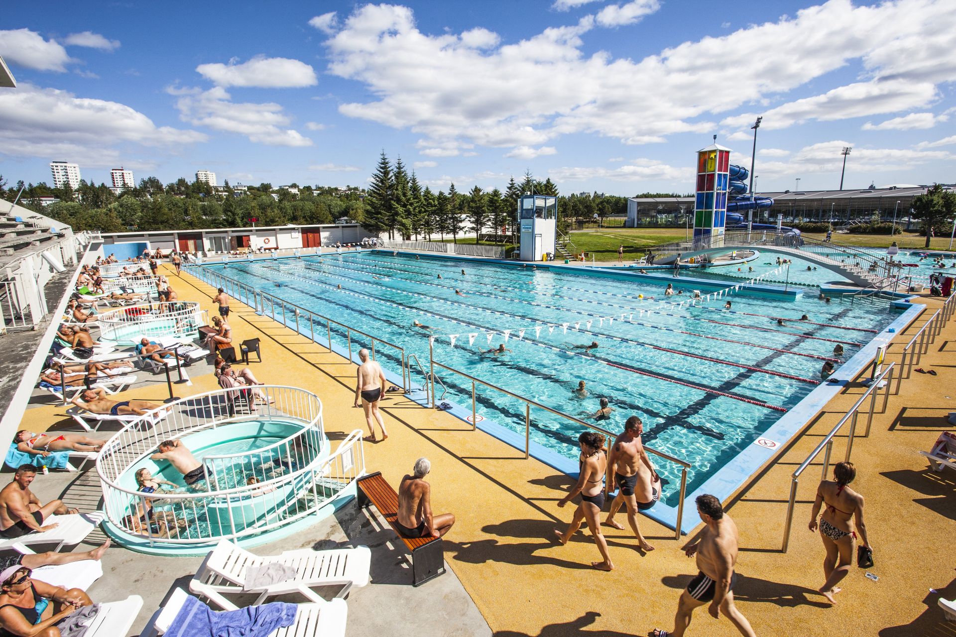 Laugardalslaug outdoor pool complex in Reykjavík with long lap lanes, hot tubs, slide tower, and bathers using the water.