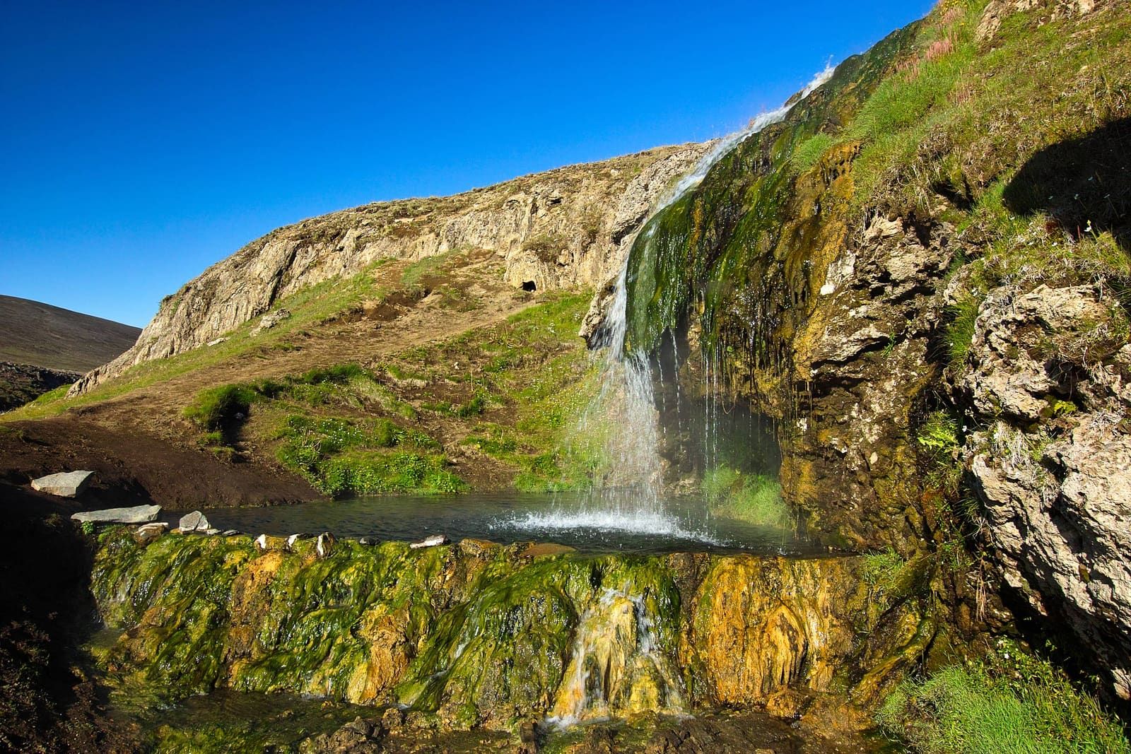 Green geothermal stream and warm waterfall flowing into a small pool in Laugarvalladalur.