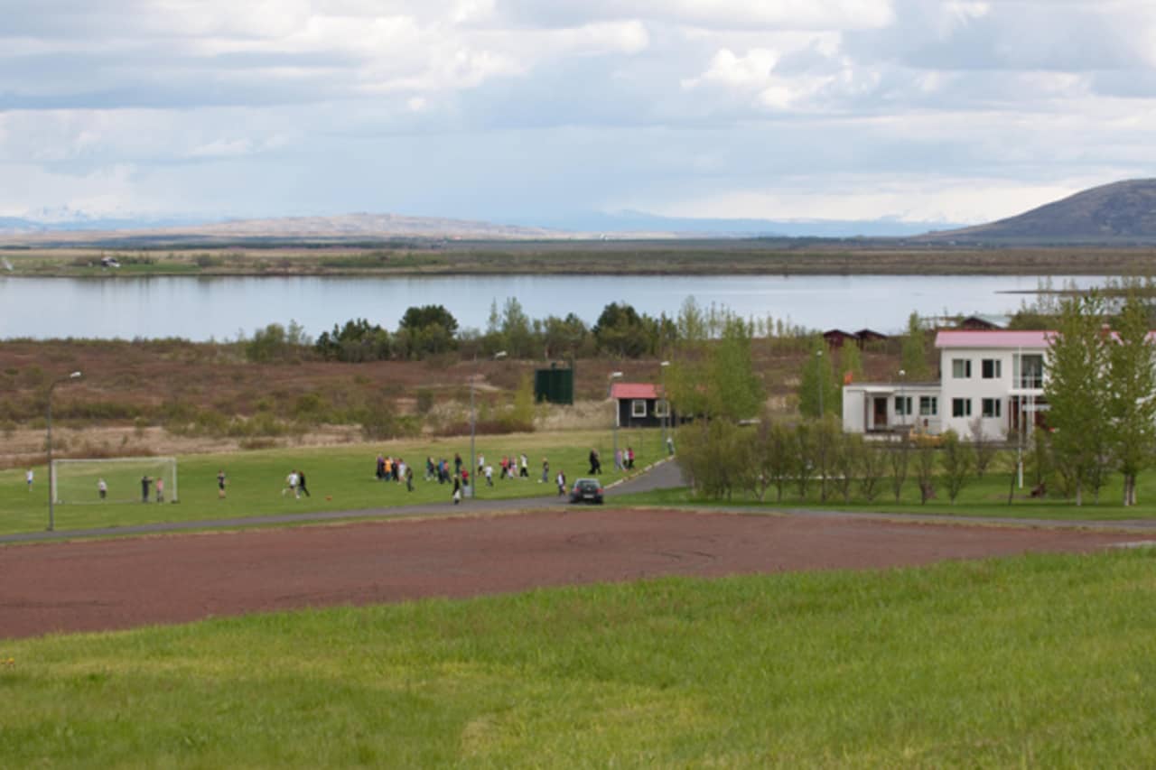 Laugarvatn village buildings and a sports field beside Lake Laugarvatn under cloudy South Iceland skies.