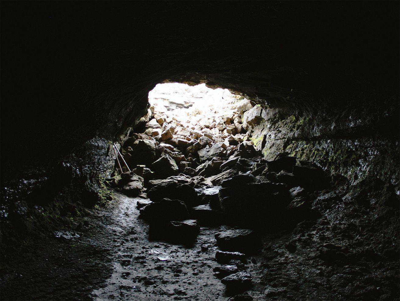 Dark Leiðarendi cave mouth with wet black lava walls and daylight over loose rocks outside.