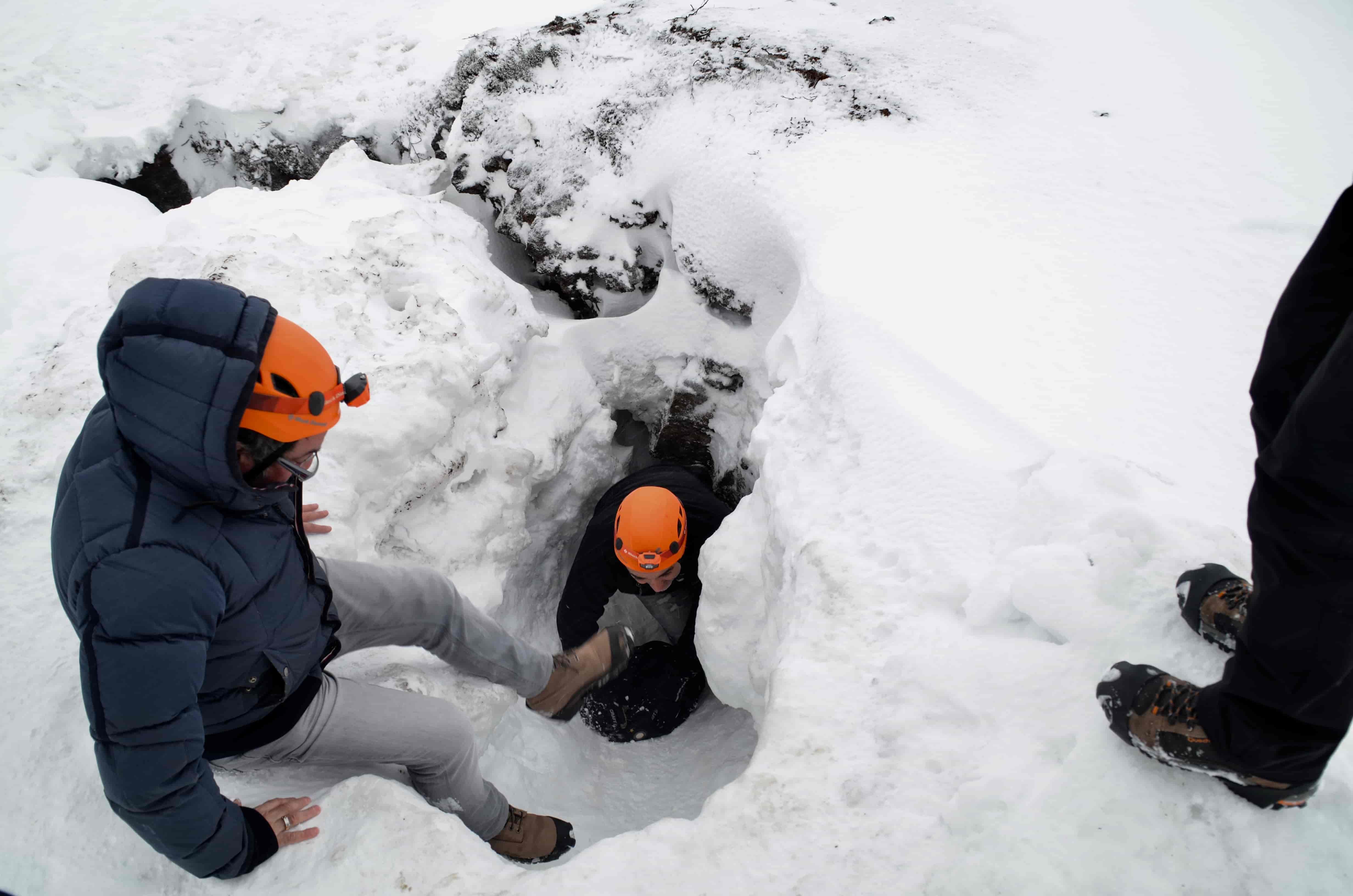 Helmeted visitors moving carefully through a snow-filled Leiðarendi cave entrance.