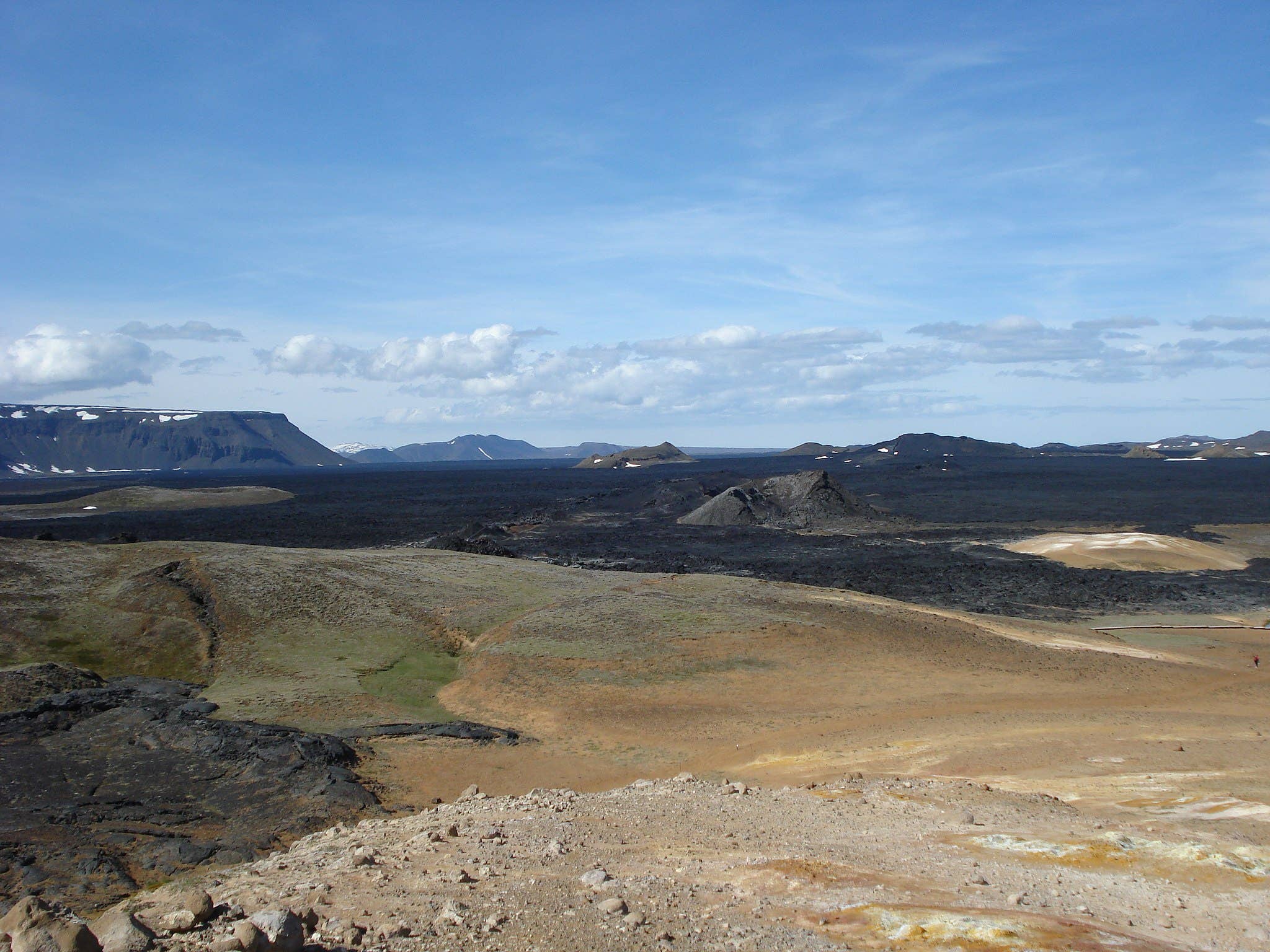 Wide view across the black lava field, crater slopes, and pale geothermal ground at Leirhnjúkur near Krafla.