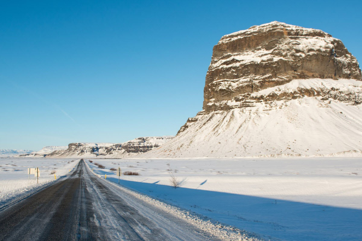 A winter road passing beside the snowy cliff face of Lómagnúpur in South Iceland.