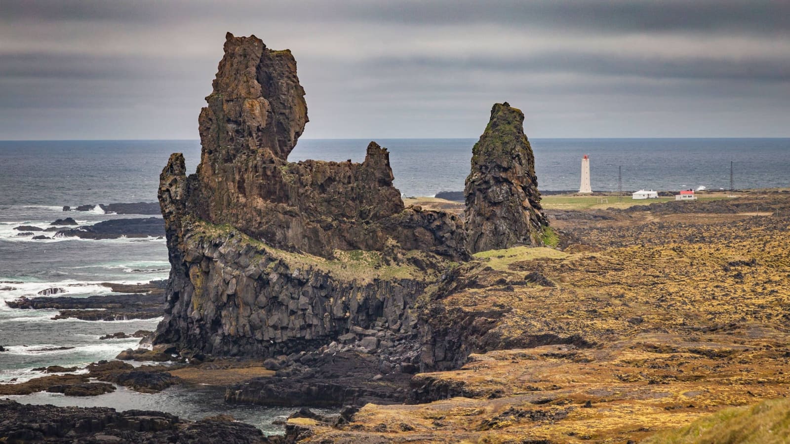 Lóndrangar sea stacks rising from the Snæfellsnes coast with Malarrif Lighthouse visible behind them.