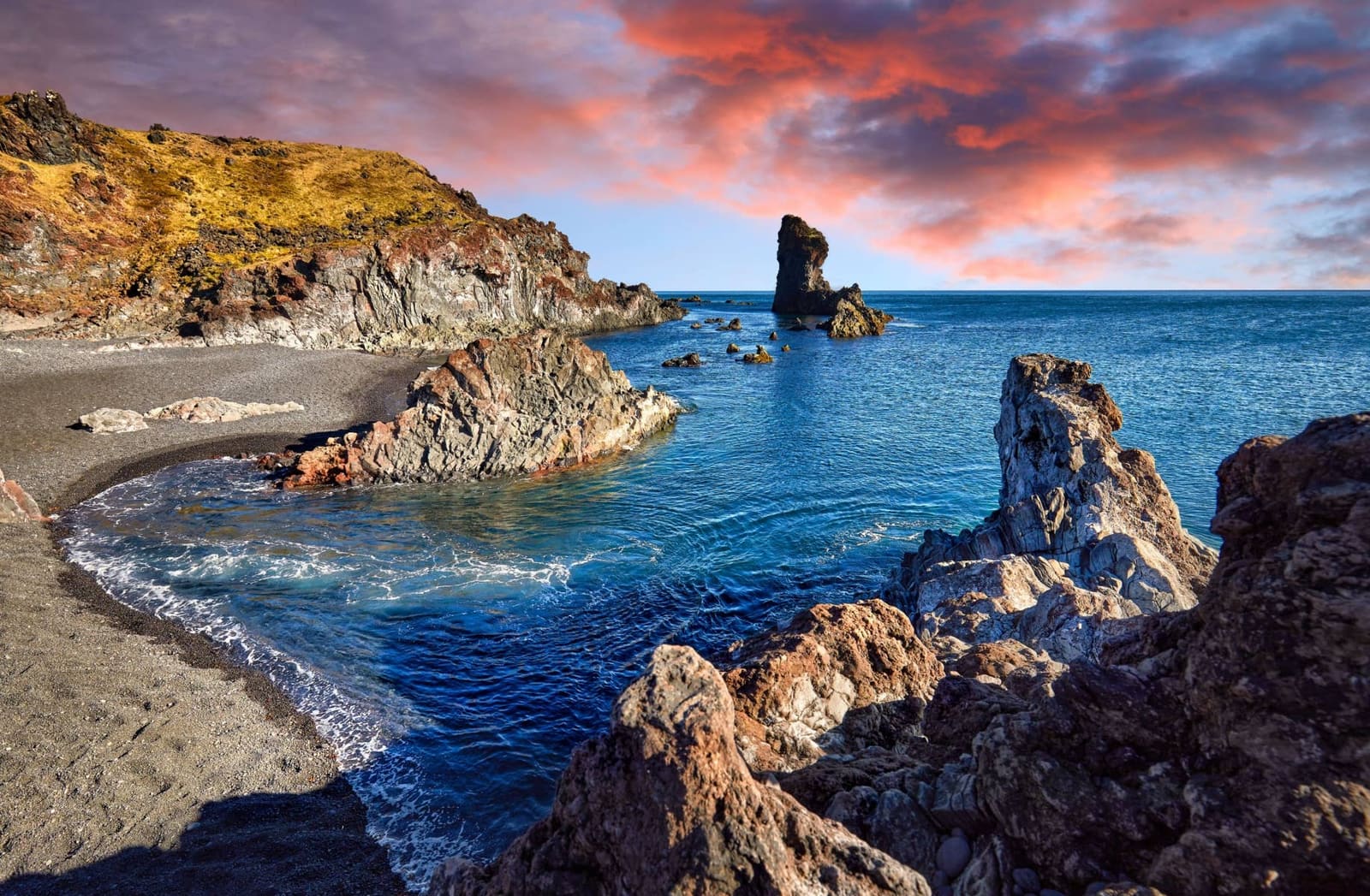 Lóndrangar basalt stacks and rocky Atlantic shoreline under sunset light.