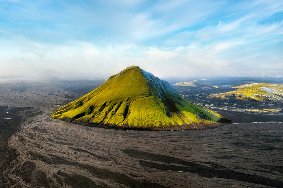 Mælifell rising above the black desert with low ridges and pale sky behind it.