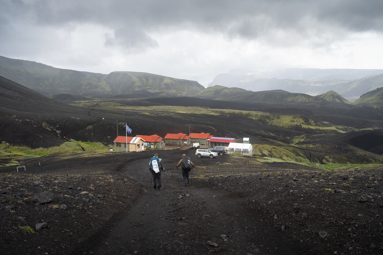 Hikers approaching the Emstrur Botnar huts across dark highland ground near Markarfljótsgljúfur.