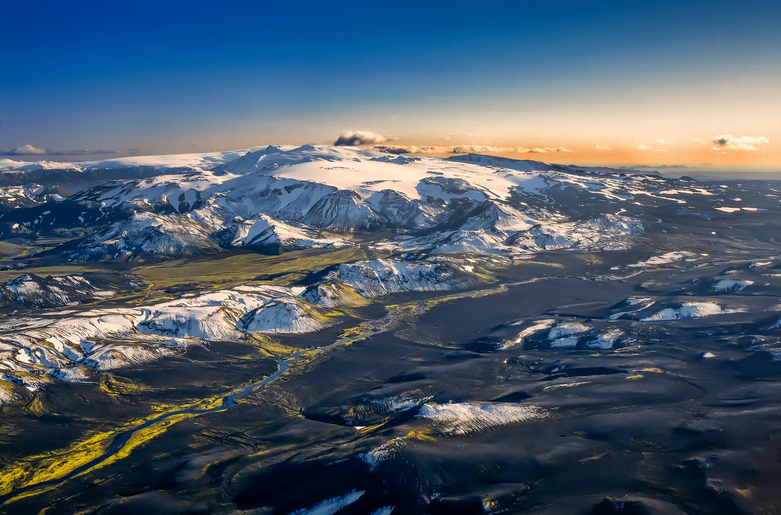 Aerial view over snowy Fimmvörðuháls and glacier-framed volcanic terrain.