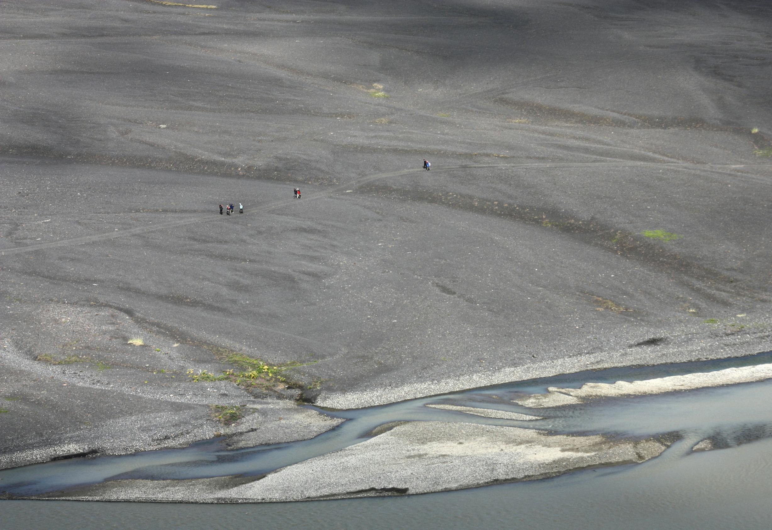 Hikers crossing dark gravel in Morsárdalur below the Morsárjökull route in Skaftafell.
