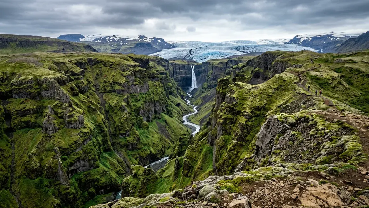 Múlagljúfur Canyon opening toward a glacier-backed skyline, with hikers visible on the rim trail.