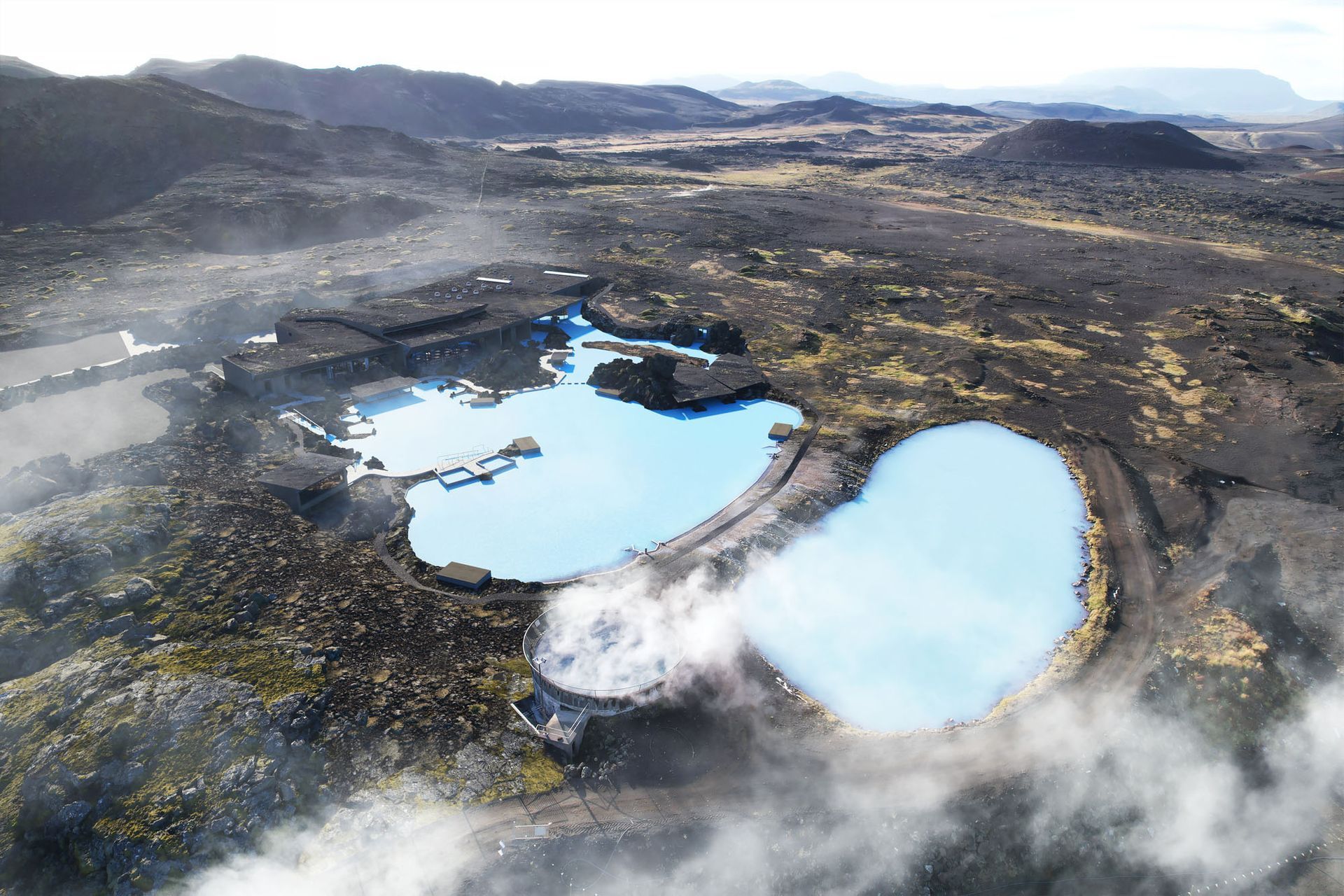 Aerial view of Earth Lagoon Mývatn pools set among dark lava fields and low mountains.