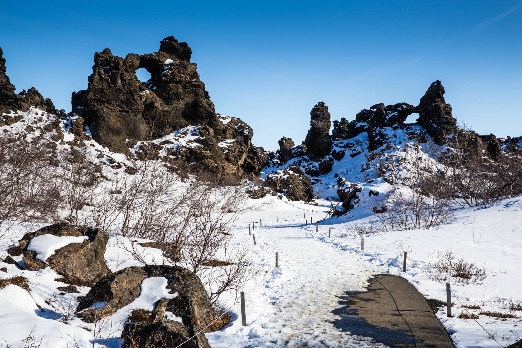 Snow-covered walking path through Dimmuborgir lava formations near Lake Mývatn.