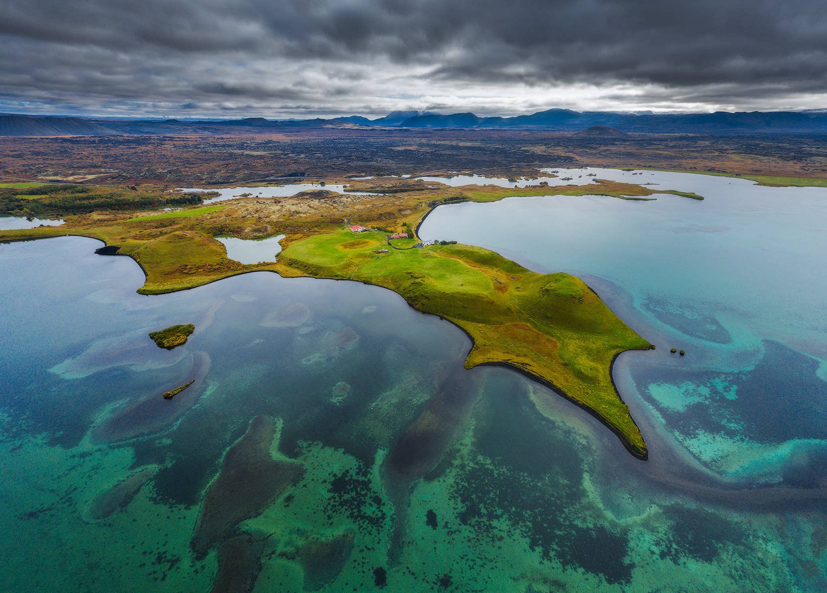 Aerial view over Lake Mývatn with green pseudocraters, shallow blue water, and volcanic hills in North Iceland.