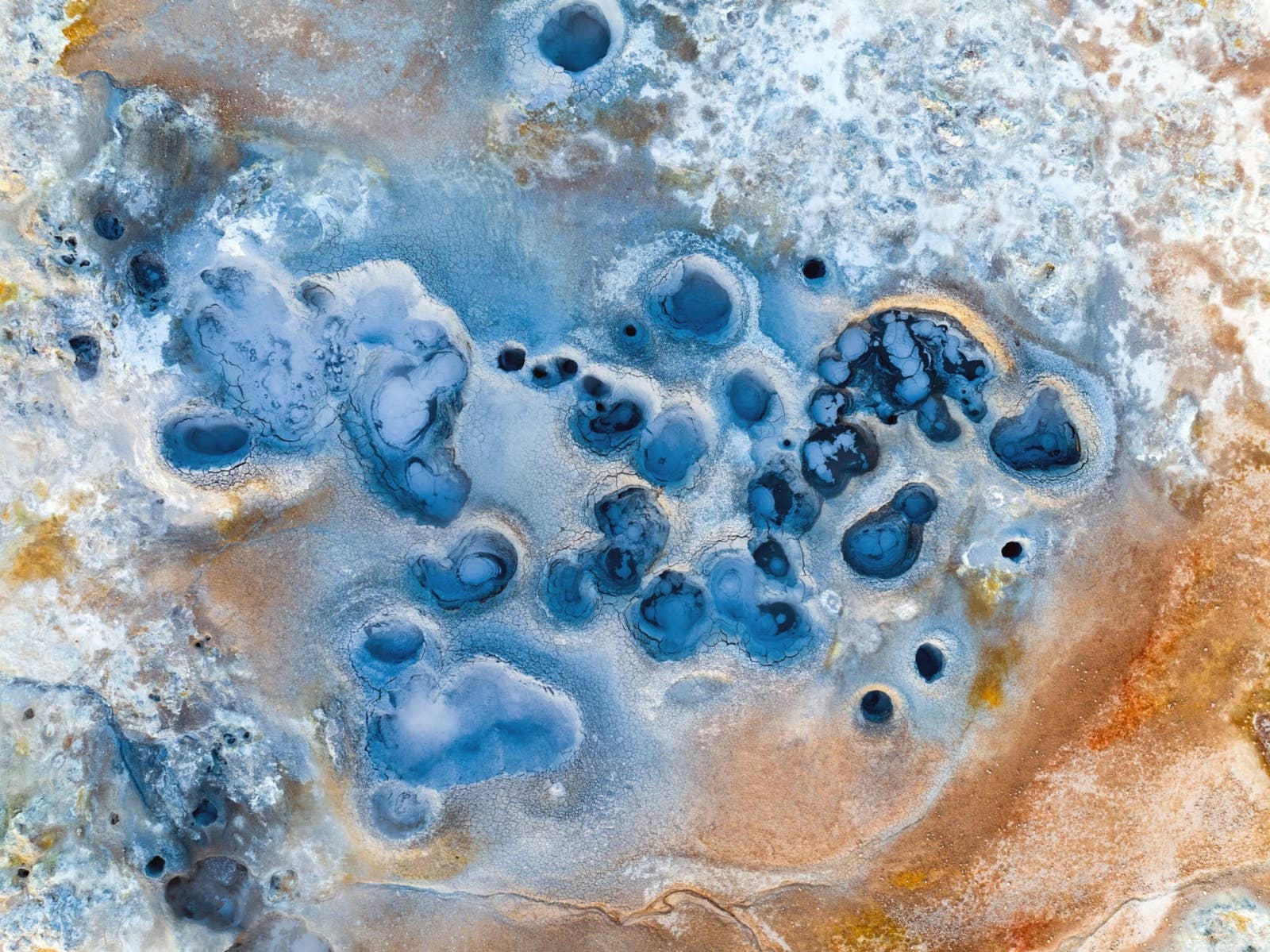 Aerial view of blue-grey mud pools and mineral-stained geothermal ground near Námaskarð Pass.