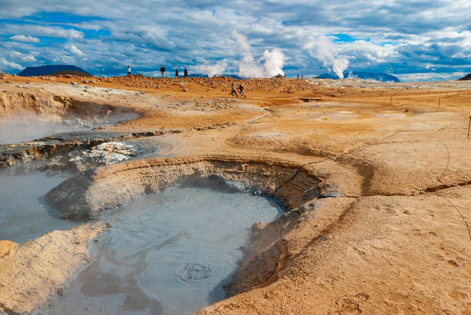 Mud pools, steam vents, marked ropes, and visitors at Námaskarð below Námafjall in North Iceland.