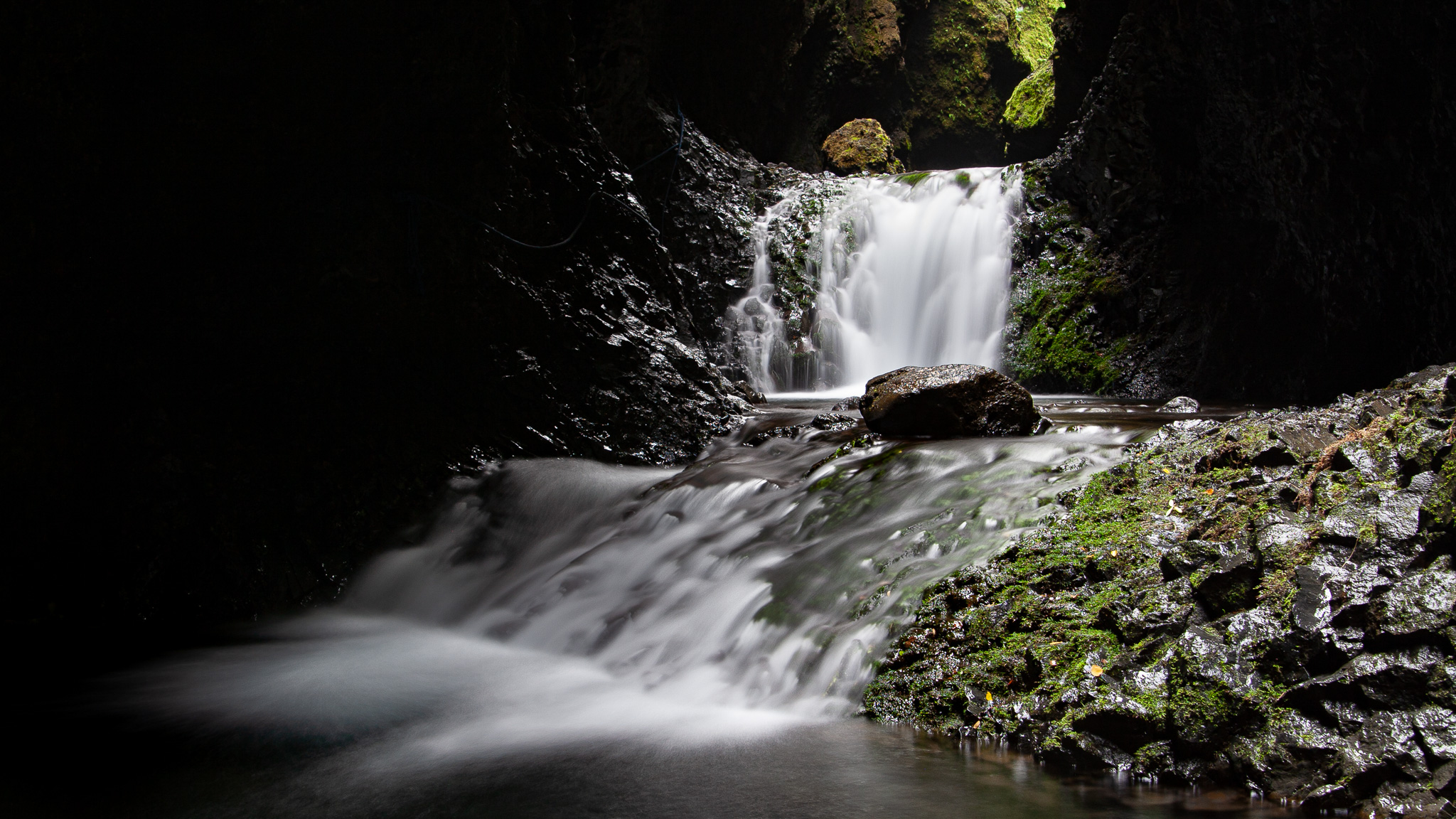 Dark mossy Nauthúsagil ravine with water flowing through the narrow canyon.