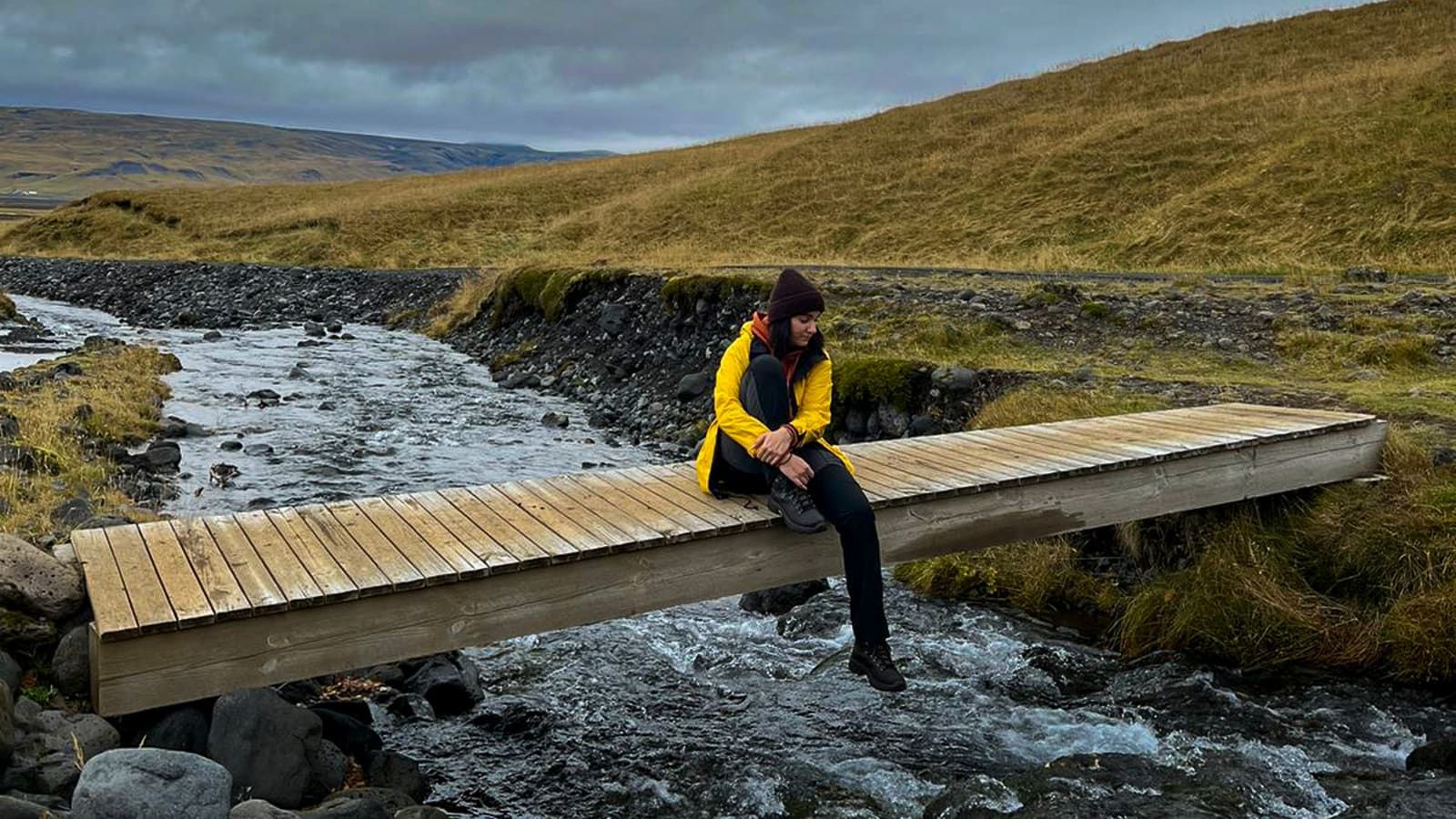 Hiker sitting on a narrow bridge over the stream at Nauthúsagil.