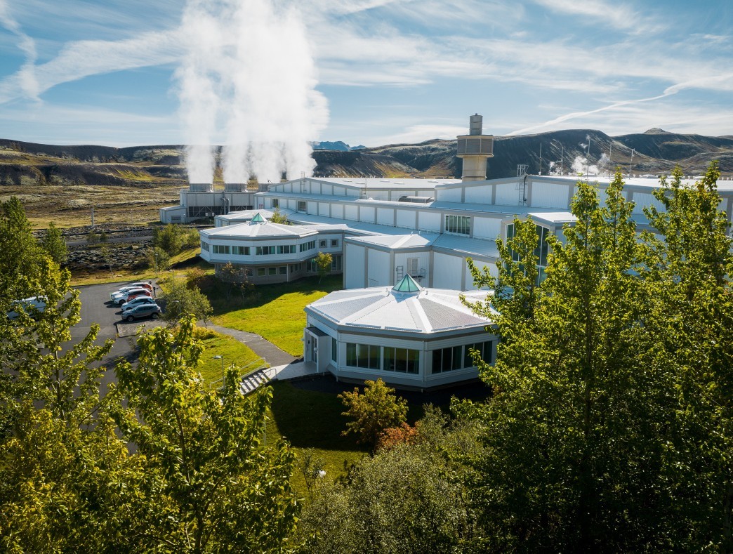 Closer view of Nesjavallavirkjun buildings with steam rising behind trees and geothermal equipment.