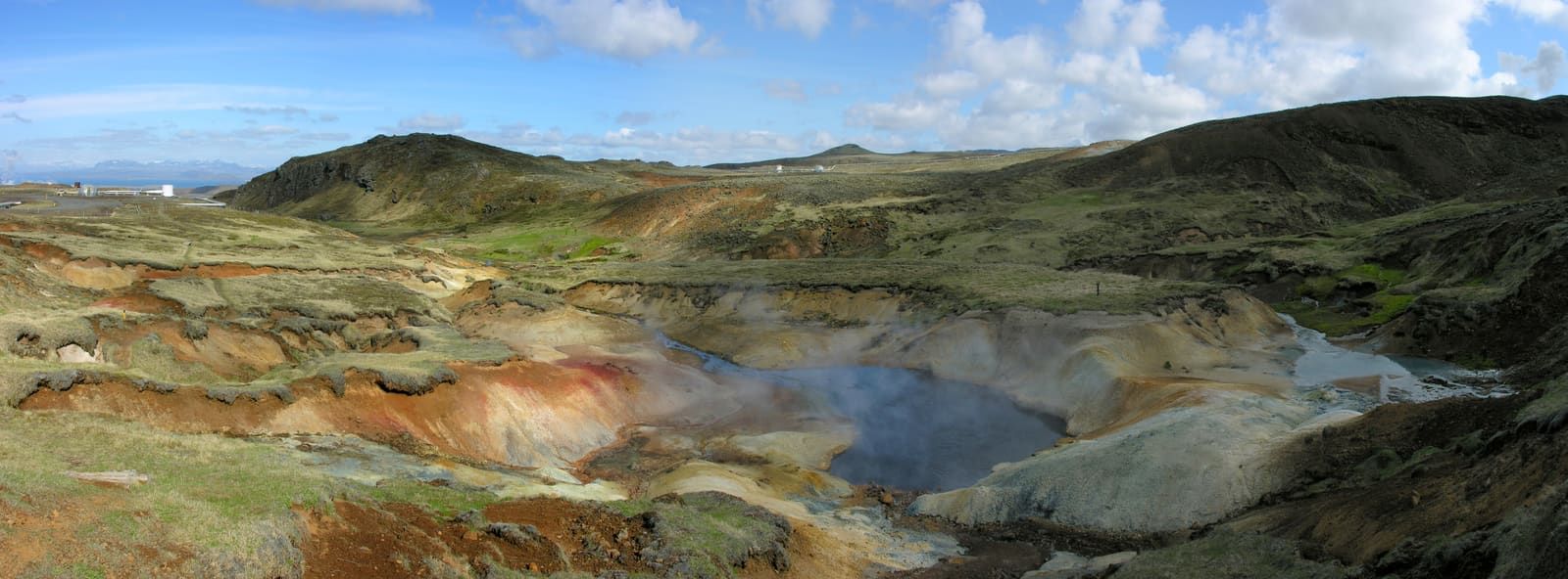 Steam rising from colorful geothermal ground above Nesjavellir with the power station in the distance.