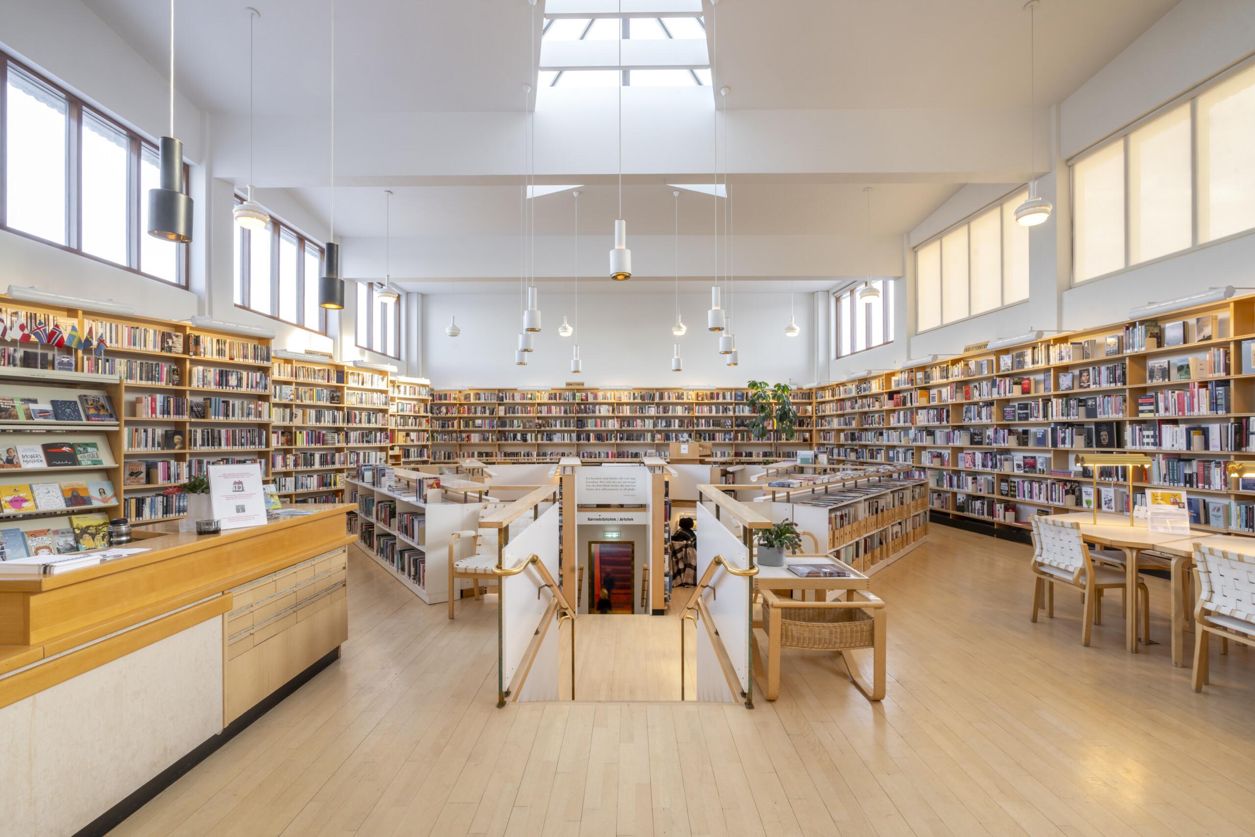 The Nordic House library in Reykjavik with pale wood shelves, hanging lamps, and a central skylight.