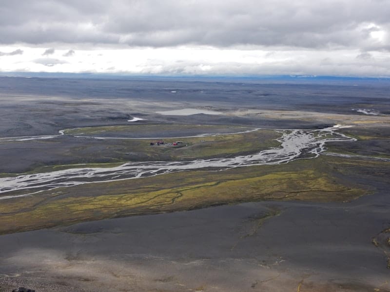 Nýidalur hut area beside braided water and dark gravel plains under low Highlands cloud.