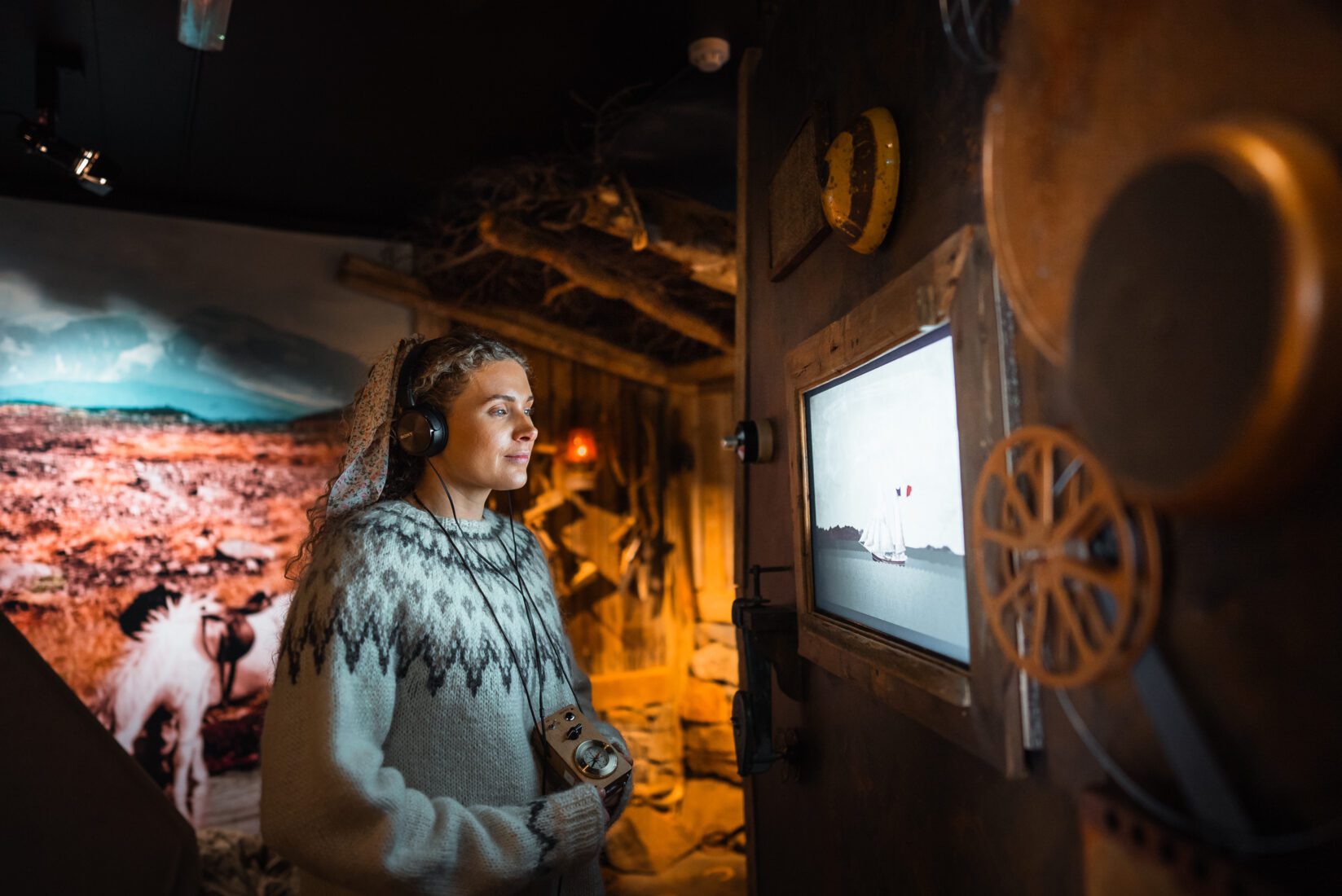 Visitor wearing headphones inside The Wilderness Center exhibition beside old-style displays and a projected landscape scene.