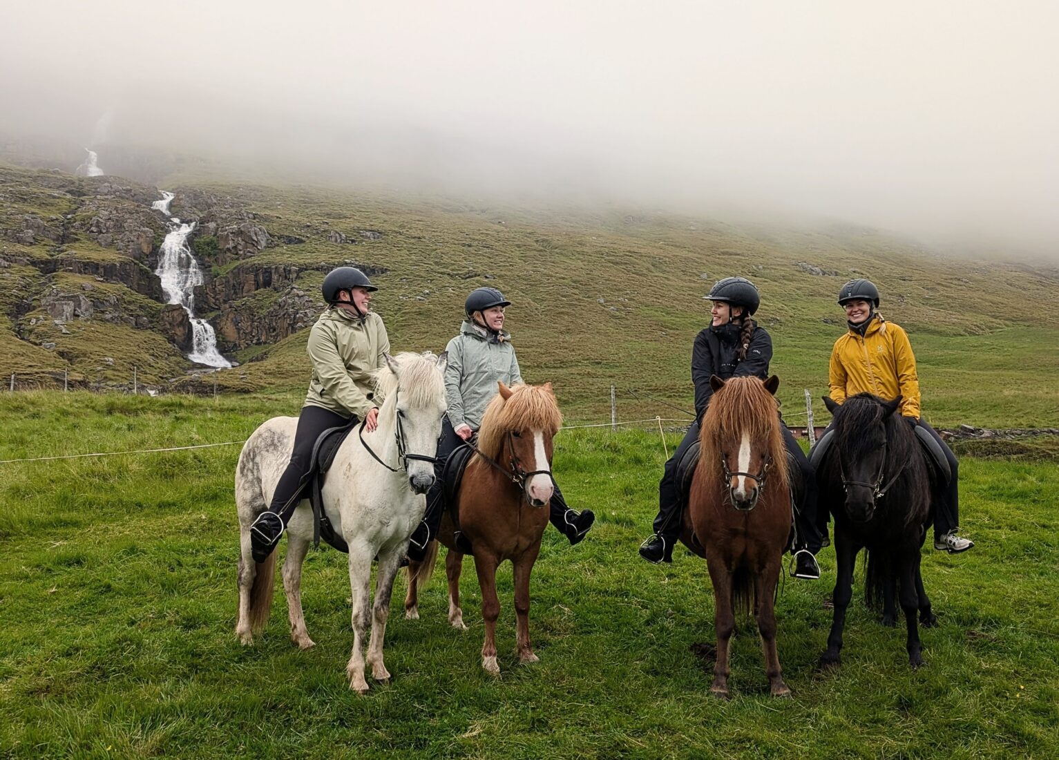 Riders on Icelandic horses near The Wilderness Center with a waterfall and misty Fljótsdalur hillside behind them.
